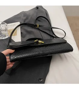 Detail of black snakeskin texture handbag with gold metal lock and adjustable strap