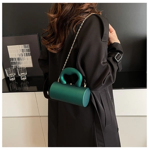 Detail of dark green acrylic cylinder bag with matte finish and gold chain strap