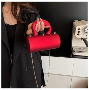 Detail of red acrylic cylindrical crossbody bag with gold chain strap and thick handle