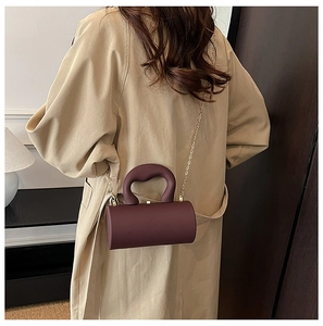 Detail of a dark purple cylindrical acrylic bag with gold chain and top handle on a trench coat