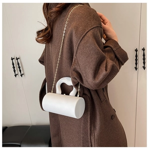Detailed side view of a white cylindrical acrylic bag with a wavy handle and gold chain strap
