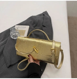 Detail of golden snakeskin embossed handbag on white bedding with a blazer and art card