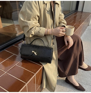 Close-up of black snakeskin texture handbag with a gold twist lock on a beige trench coat