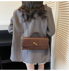 Detail of brown snakeskin crossbody bag with golden knot clasp worn by a model