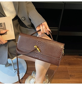 Detail of dark brown faux snake skin handbag with golden knot clasp in a lifestyle setting