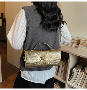 Detailed close-up of golden snakeskin embossed texture and metal twist knot on the handbag