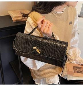 Detail of glossy black snake skin texture handbag with golden cylindrical mechanical lock