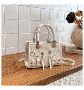 Detailed view of white motorcycle bag with braided handle and silver studs on wood