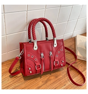 Detail view of red rivet handbag with woven handle on a rustic wooden table surface