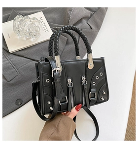 Detailed view of black rivet handbag with woven handle on a grey suit jacket background