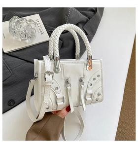 Close-up of white motorcycle handbag with silver rivets and woven handles on a desk