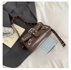 Detail of dark brown rivet handbag with silver buckle over a grey suit backdrop