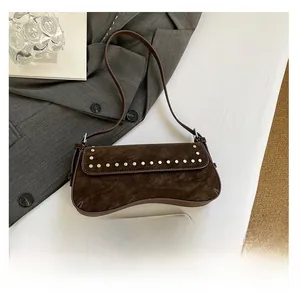Detail of brown suede shoulder bag with silver rivet trim beside a smartphone for size