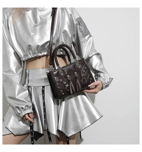 Detail of dark brown punk style handbag with rivets, woven handles and metal buckles