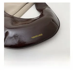 Détail de la texture en cuir verni brillant marron foncé et logo sur le sac croissant