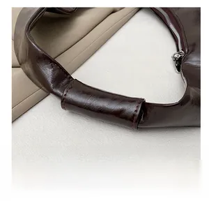 Détail des poignées renforcées et coutures sur le sac demi-lune marron brillant