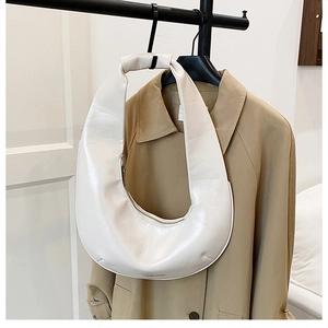 Détail du sac hobo crème sur un trench-coat montrant la texture en cuir lisse et brillant