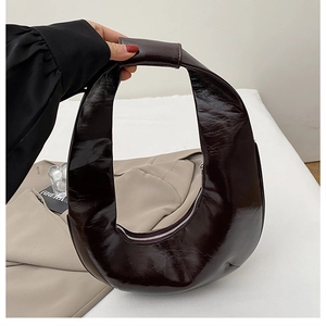 Détail du sac croissant marron foncé brillant montrant la texture du cuir verni