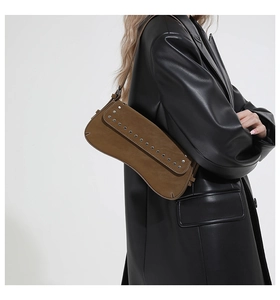Detail of vintage brown suede shoulder bag with rivets worn by model in a black leather blazer