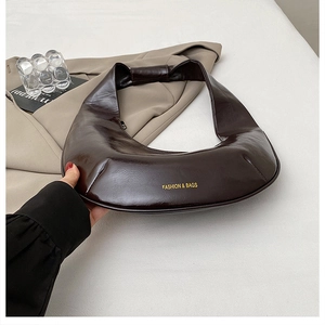 Détail du sac demi-lune marron brillant avec lettrage doré et large bandoulière élégante
