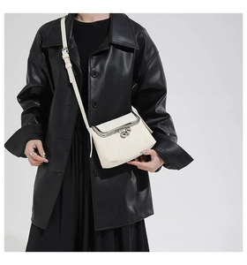 Close-up of minimalist cream crossbody bag with silver metal kiss-lock clasp detail