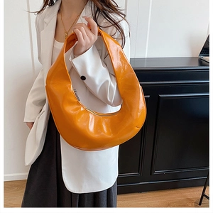 Détail du sac demi-lune en cuir brillant orange vif avec une large bandoulière élégante