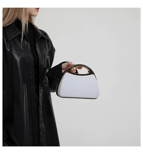 Close-up of white sequin shell evening bag with gold circular metal handle held by model
