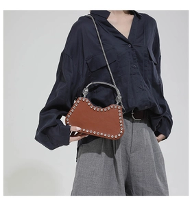 Détail du sac en cuir marron avec rivets argentés et poignée métallique courbe