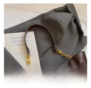 Detalle de bolso de cuero marrón oscuro con hebilla cuadrada dorada sobre blazer gris