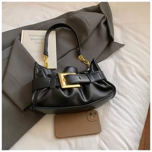 Detalle de bolso medialuna negro con hebilla dorada y cadena sobre ropa de cama