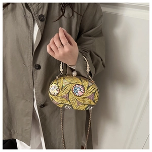 Detalle de bolso de noche con lentejuelas, bordado de hojas doradas y asa de metal