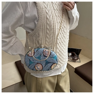 Detalle de un bolso de fiesta de lentejuelas azules con bordado floral y cadena dorada