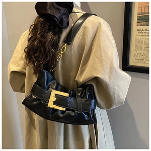 Detalle de bolso nube plisado negro con hebilla dorada sobre una gabardina beige chic