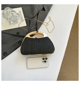 Mini sac à main tissé noir avec poignée dorée et chaîne à côté d'un smartphone blanc