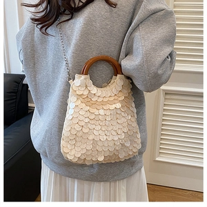 Details der beigen Pailletten-Muscheltasche mit runden Holzgriffen und Silberkette