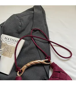 Detail of wine red woven crescent bag with gold metal handle on a grey suit jacket