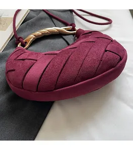 Close-up of burgundy woven crescent bag with decorative gold twisted metal handle