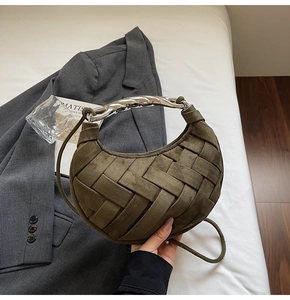Detail of dark olive woven crescent bag with silver spiral handle on a white bed