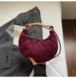 Close-up of burgundy woven crescent bag with gold spiral metal handle and suede texture
