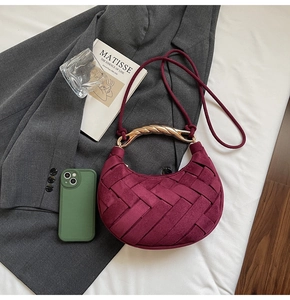 Detail of burgundy woven crescent bag with gold handle on a grey suit jacket