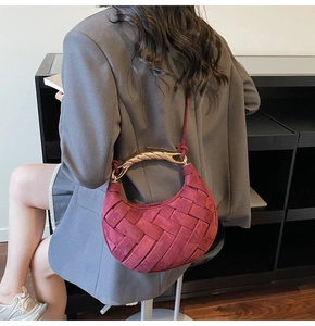 Detail of burgundy woven crescent bag with gold-tone twisted handle on grey blazer