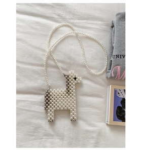 Detailed view of handmade pearl woven horse-shaped handbag on white textured fabric