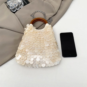 Elegant shell-style handbag with wood handle and sequins beside a smartphone for scale