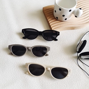 Three pairs of stylish cat-eye sunglasses in black, grey and beige on a modern desktop