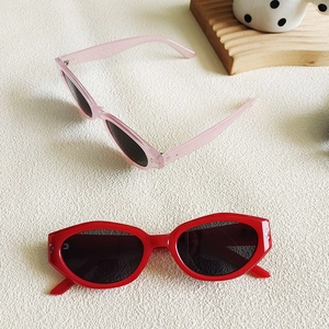 Detail of pink and red cat-eye sunglasses with silver rivets on wavy wooden tray