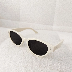 Detail of cream white cat eye sunglasses with metal rivets on a soft white texture