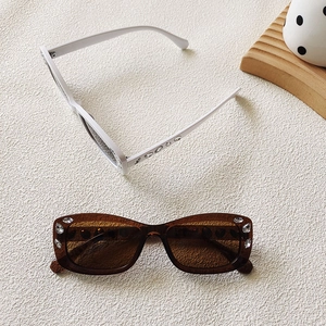Retro small frame sunglasses with rhinestones in white and amber colors displayed on beige