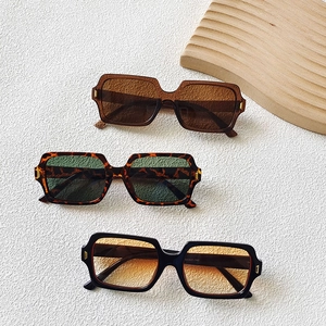 Three pairs of vintage square sunglasses in tortoiseshell, black and brown frames on a textured background
