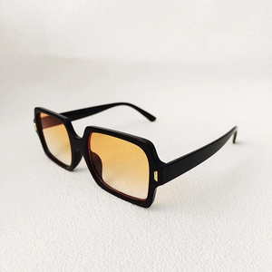 Detail of square black sunglasses featuring orange gradient lenses and gold accents