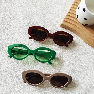 Retro oval cat eye sunglasses in burgundy, green, and beige colors on a textured surface
